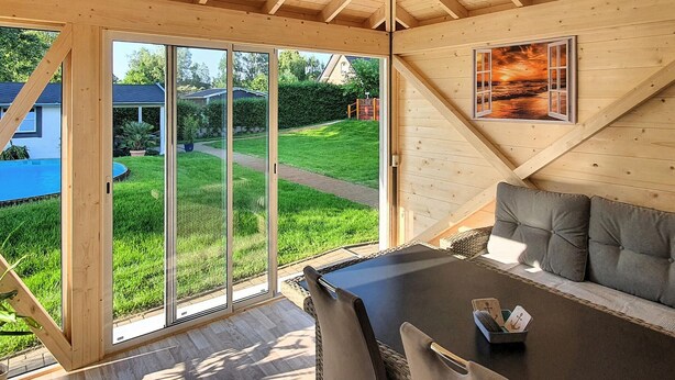 A cozy wooden interior with a large sliding glass door leading to a green lawn and a pool. - Ferienwohnung Neppermin/Usedom (Neppermin/Usedom)