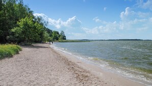 A sandy beach with a calm lake, surrounded by trees and a clear sky. - Ferienwohnung Neppermin/Usedom (Neppermin/Usedom)