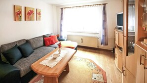 Una sala de estar acogedora con un sofá gris, una mesa de centro de madera y un televisor sobre un mueble de madera.