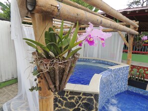 Un bain à remous entouré de pierres, bordé d’une structure en bambou, et un petit espace jardin agrémenté de plantes et de fleurs.