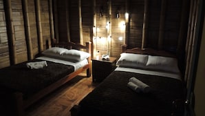 Deux lits simples avec des cadres et des têtes de lit en bois, une table de chevet avec une lampe et un mur recouvert de lambris verticaux en bambou.