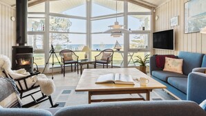 A cozy room with a large window, a fireplace, a sofa, and a table with a book and mug. - Awesome home in Sjællands Odde (Sjællands Odde)