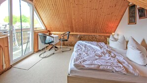 Quarto com cama grande, escrivaninha, duas cadeiras e janela com vista para um jardim.