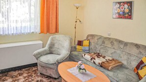 Una sala de estar con un sillón gris, un sofá con cojines estampados, una mesa de centro redonda de madera y un cuadro en la pared.
