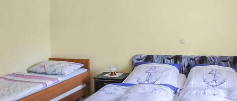 Une chambre avec deux lits, dont l’un est doté d’une tête de lit en bois et l’autre d’une tête de lit recouverte d’un tissu gris. On y trouve une petite table de chevet avec une lampe et une boîte à mouchoirs.