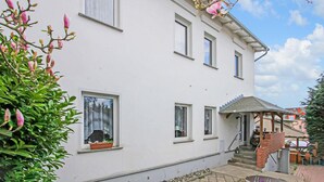 Ein zweistöckiges weißes Gebäude mit vielen Fenstern, einer kleinen Veranda und einer Treppe, die zu dem oberen Stockwerk führt.