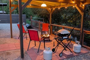 Un espace extérieur abrité, équipé d’un barbecue, de chaises et d’un foyer.