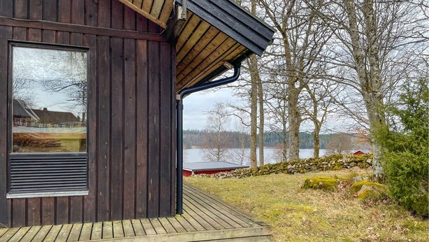 Una cabaña de madera con un amplio ventanal y una terraza con vista a un lago.