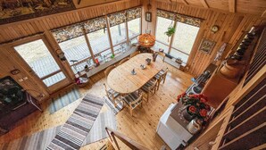 Amplia habitación con una gran mesa de madera para comer, varias ventanas y una escalera que sube a otro nivel.