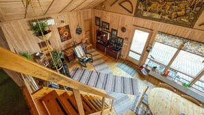 Amplio interior de madera con una escalera, comedor y sala de estar con un ventanal y obras de arte.