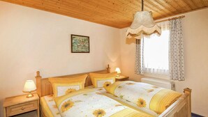Une chambre à coucher avec une tête de lit en bois, deux tables de chevet avec des lampes, un lit avec une literie à motifs floraux, une lampe suspendue, une fenêtre avec des rideaux et un tableau accroché au mur.
