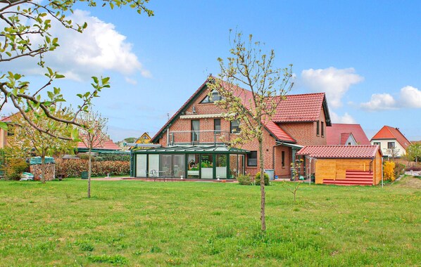 A large brick house with a red roof, a glass conservatory, and a small wooden structure in the yard.