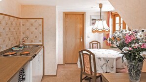 A compact kitchen with a wooden countertop and a sink, a dining area with a table and chairs, and a vase with flowers on the table.