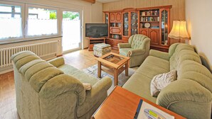 A living room with a sofa set, a coffee table, a television, a bookshelf, and a window with curtains. - Ferienwohnung Zinnowitz Seebad (Zinnowitz (Seebad))