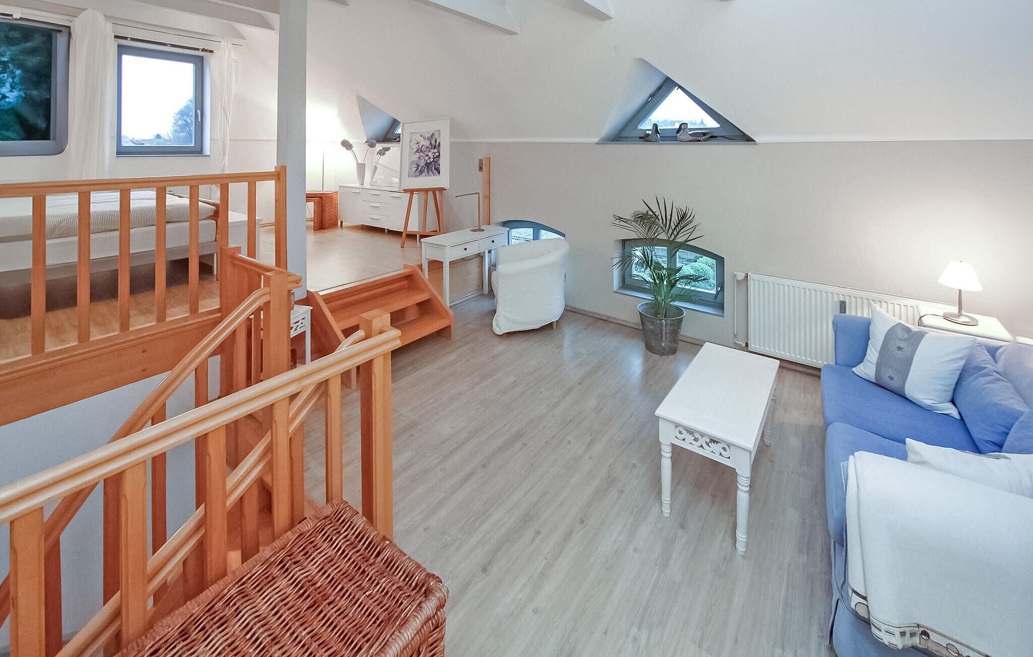 Een ruime woonruimte met een houten trap, een blauwe bank, een witte salontafel en een potplant.