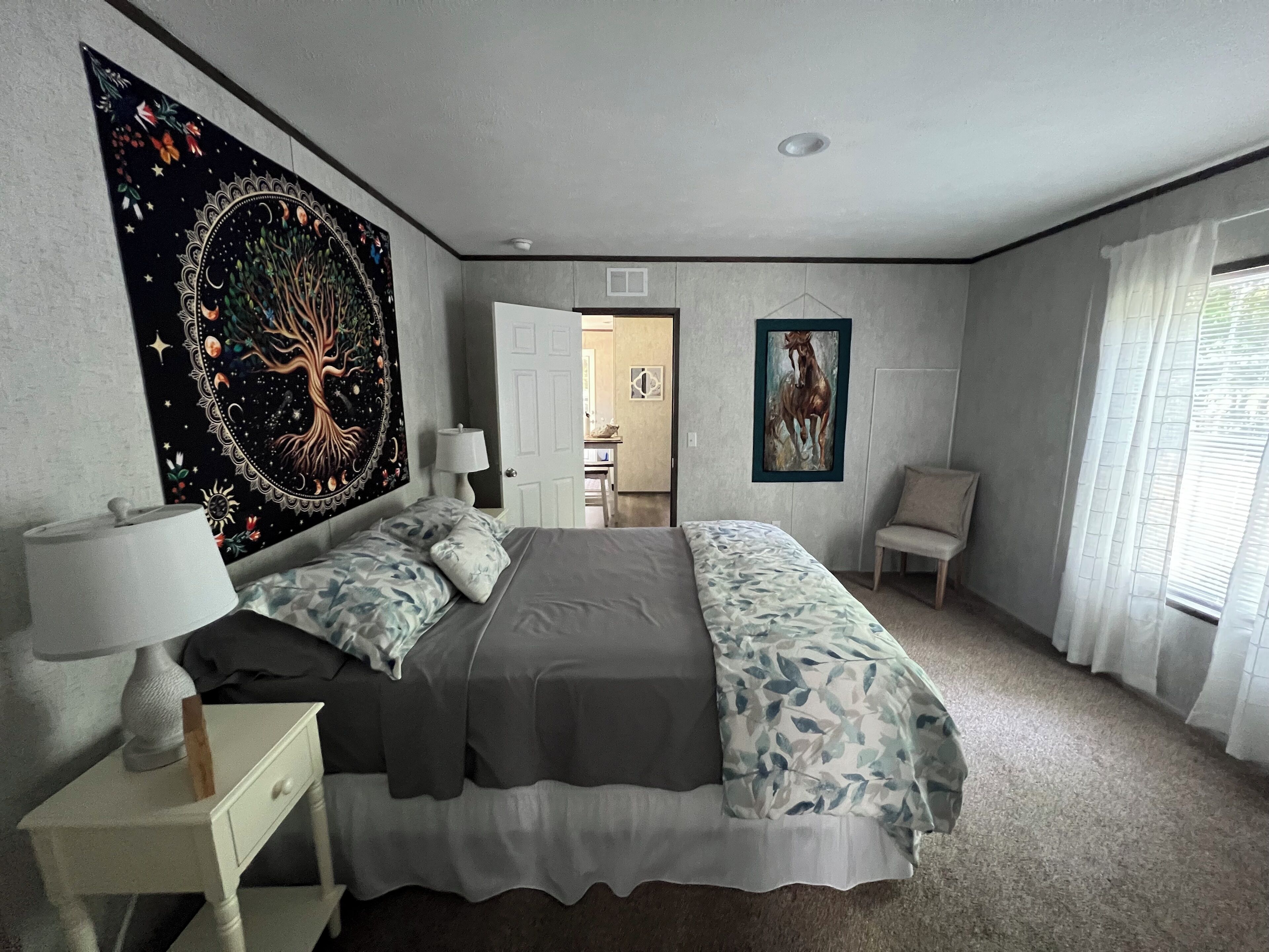 Ein Schlafzimmer mit Bett, Nachttischen, einem großen Wandteppich, einem gerahmten Gemälde und Blick auf einen Flur.