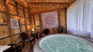 Una cabaña de madera con jacuzzi, mobiliario de mimbre y luces colgantes.