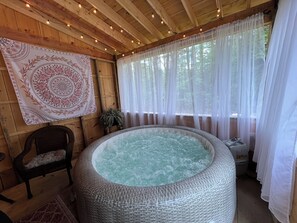 A wooden cabin with a hot tub, a chair, and a tapestry. - Relaxing tranquil setting, hot tub, fire pit; Pet friendly. (Middle Grove)