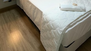 Un lit bien fait, avec du linge de lit blanc, une table de chevet avec une lampe et un plancher en bois.