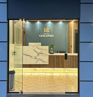 Zona de recepción de un hotel con diseño moderno, que incluye un mostrador de mármol, un logotipo sobre el mostrador y una planta en el mostrador.
