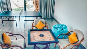 Una habitación con una mesa, sillas, un sillón de peluche azul y una mesa de futbolín.