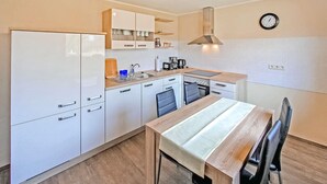 A compact kitchen with white cabinets, a wooden dining table, and a single wall clock. - Nice apartment in Mirow with WiFi (Mirow)