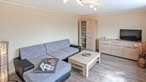 A modern living room with a grey sofa, a wooden coffee table, a TV on a wooden cabinet, and a floor lamp. - Nice apartment in Mirow with WiFi (Mirow)