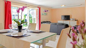 Un coin repas avec une table dressée pour deux personnes, un canapé, un téléviseur et une plante en pot.