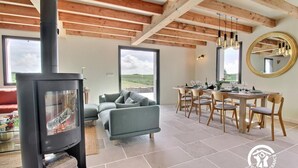 A modern living room with a fireplace, a sofa, a dining area with chairs, and large windows offering a view of the outdoors. - Villa Valérie - Locmaria (LOCMARIA)