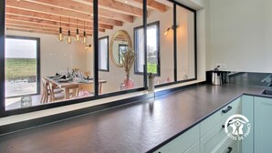 A modern kitchen with a large window, wooden ceiling beams, and a view of the outdoors. - Villa Valérie - Locmaria (LOCMARIA)