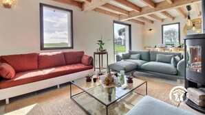 A modern living room with a red sofa, a grey sofa, and a glass coffee table. There is a fireplace and a large window in the background. - Villa Valérie - Locmaria (LOCMARIA)