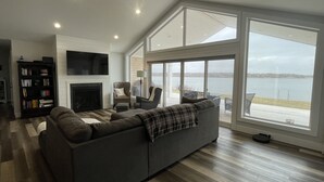 Ein geräumiges Wohnzimmer mit Kamin, großem Fenster mit Blick auf ein Gewässer und modernem Design.
