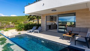 Zona d'una piscina moderna a l'aire lliure, amb cuina integrada i seients.