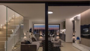 Un saló modern amb un sofà, butaques i una taula de centre. S'hi veu una escala a l'esquerra i una zona de cuina a la dreta.