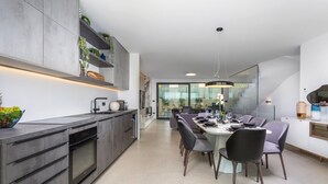 Cuina moderna amb forn incorporat, zona de menjador amb taula rodona i cadires, i una finestra gran que deixa entrar llum natural.