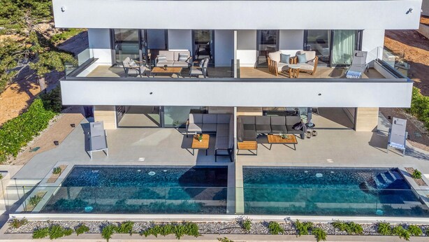 Una casa moderna de dos pisos amb una gran piscina coberta per vidre i zones d'estar a l'aire lliure.