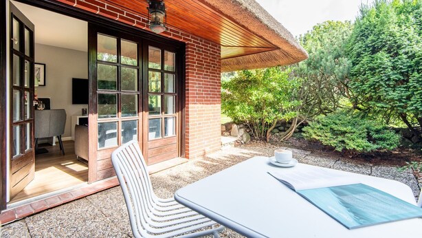 A patio with a table and chairs, a brick wall, and a door leading to an interior space. - Watt. Familie. Reet. - Erich Johannsen Wai (Keitum)