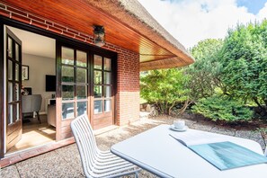 Eine Terrasse mit Tisch und Stühlen, eine Ziegelwand und eine Tür, die zu einem Innenraum führt.