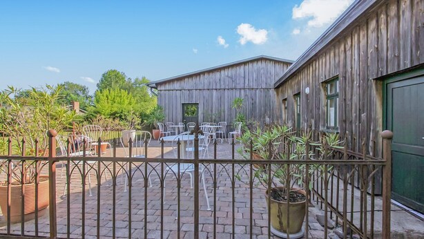 A rustic outdoor seating area with metal chairs and tables, surrounded by potted plants and a wooden fence. - Ehemaliges Farmhaus Lehsten (Lehsten)