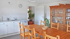 A kitchen with white cabinets, a wooden dining table with chairs, a potted plant, and a cabinet with glass doors. - Ehemaliges Farmhaus Lehsten (Lehsten)