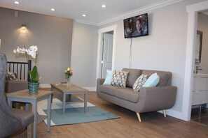 A modern living room with a grey sofa, wooden coffee table, and a TV mounted on the wall. - Central House (Chilliwack)