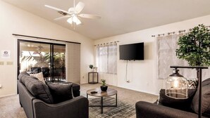 A modern living room with a sofa, coffee table, and a TV. - Sunny Oasis 4BR Pool Home with Game Room (Mesa)
