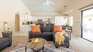 A modern living room with a sofa, coffee table, and a dining area in the background. - Sunny Oasis 4BR Pool Home with Game Room (Mesa)