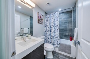 Een moderne badkamer met een witte wastafel, toilet en douche met een bloemen gordijn.