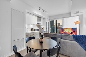 Een moderne keuken met witte kasten, een eettafel met stoelen en een zithoek met een bank en een open haard.