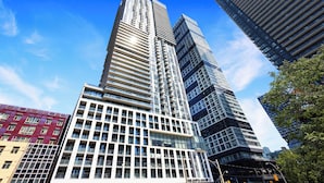 A modern high-rise building with a glass facade, multiple floors, and a prominent entrance. - Panorama Suites (Toronto)