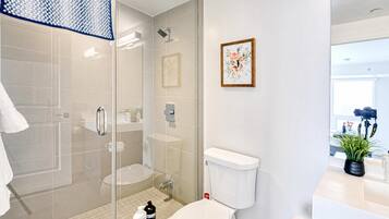 Casa de banho moderna com chuveiro em cabine de vidro, sanita e lavatório com espelho.