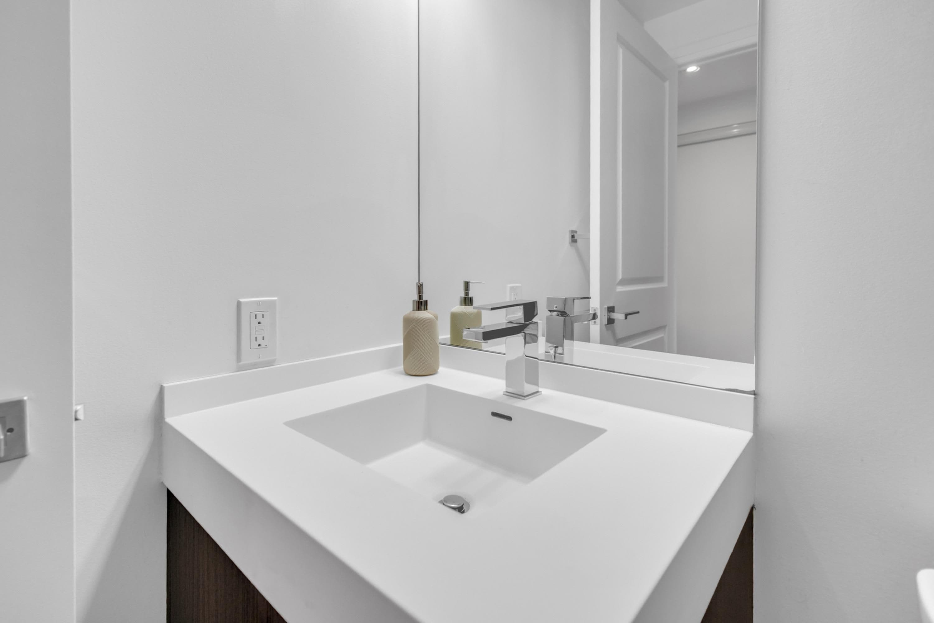 A modern bathroom with a white sink, a mirror, and a towel dispenser.