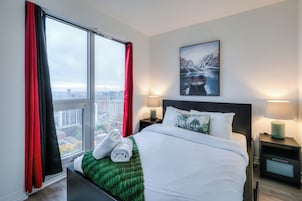 Een hotelkamer met een groot bed, twee bedlampen, een nachtkastje, een groene plaid en een raam met rode gordijnen.