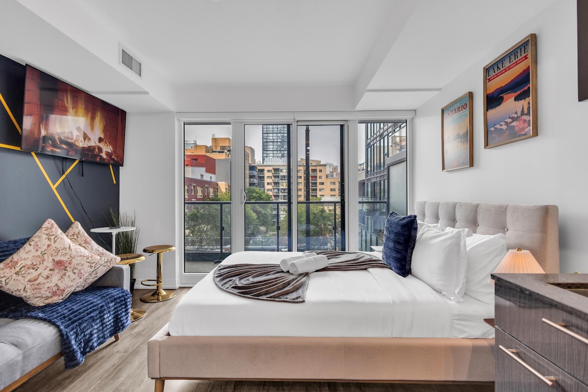 Un dormitorio moderno con una cama grande, vistas de la ciudad a través de ventanales del suelo al techo y un cuadro en la pared.